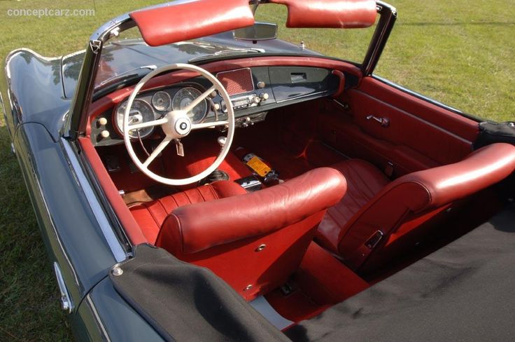 the interior of an old car with red leather seats and steering wheel, on display in a field