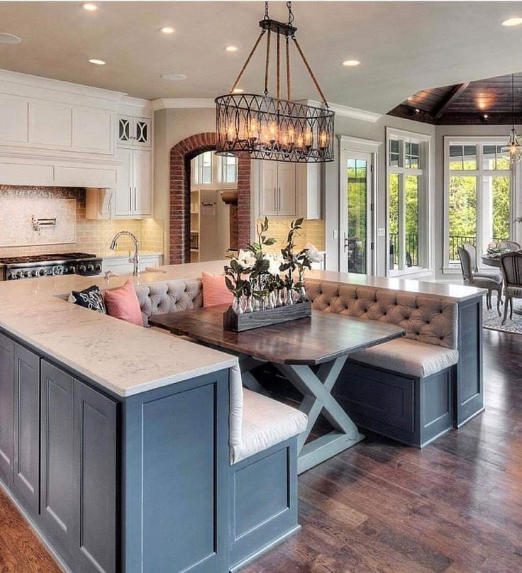 a large open concept kitchen and dining room with wood flooring, white cabinets, an island bench, and chandelier hanging from the ceiling