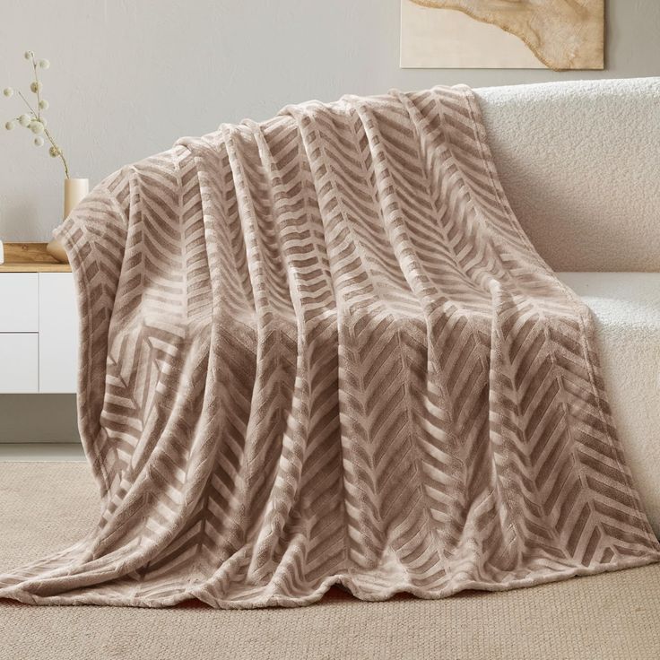 a couch with a blanket on top of it next to a white table and vase