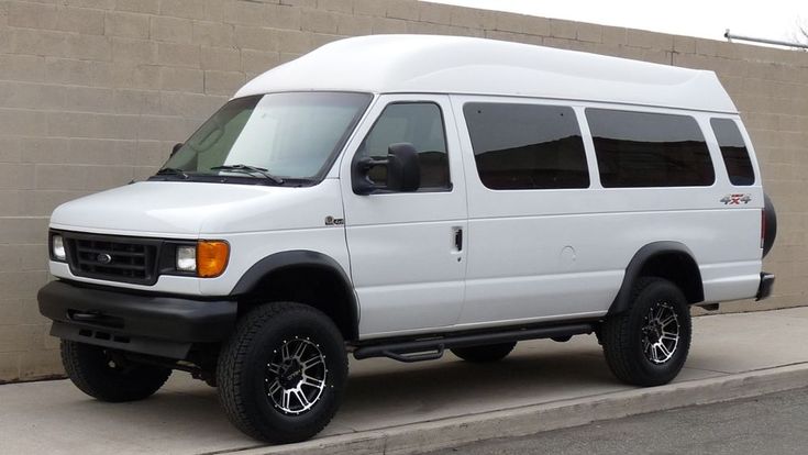 the white van is parked on the side of the road near a wall and sidewalk