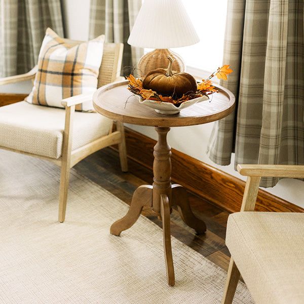 a small table with some pumpkins on it in front of two chairs and a lamp