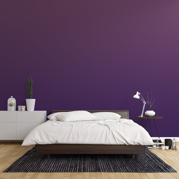 a bed sitting on top of a wooden floor next to a purple wall