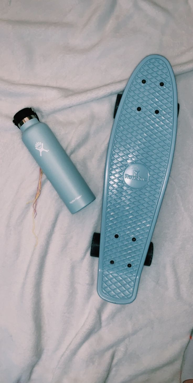 a blue skateboard laying on top of a white sheet next to a water bottle