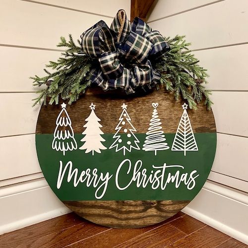 a merry christmas sign hanging on the side of a house with pine trees and evergreens