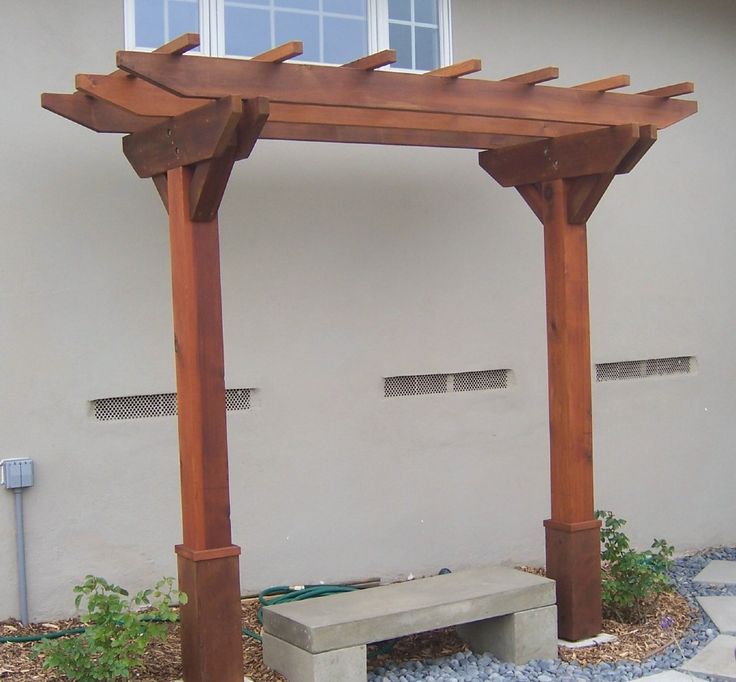 a bench under a pergolated wooden arbor in front of a house