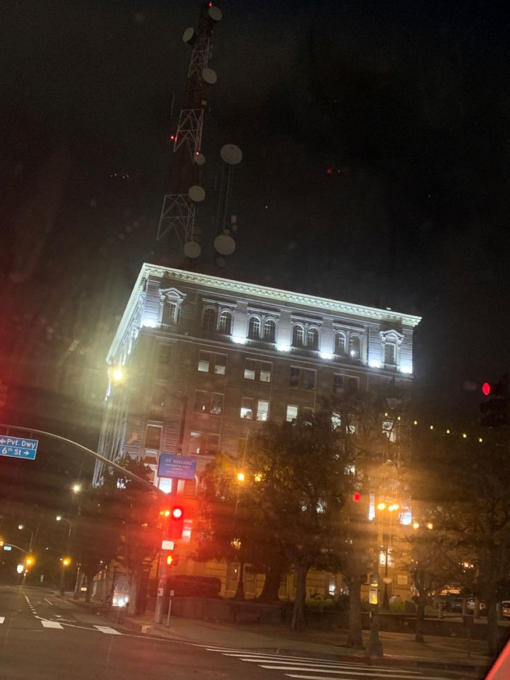 an old building is lit up at night with street lights in the foreground and traffic