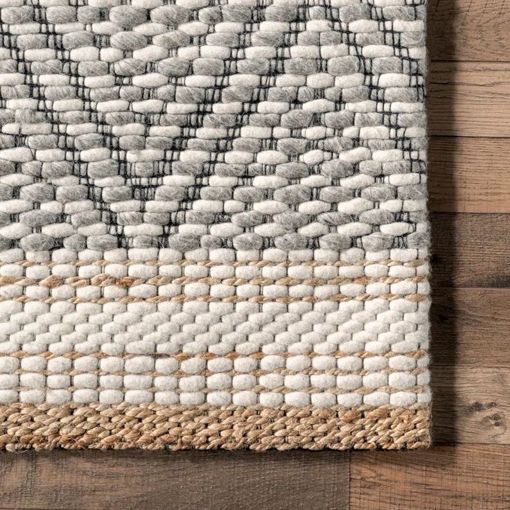 an area rug with white and grey squares on top of wooden flooring next to a wall