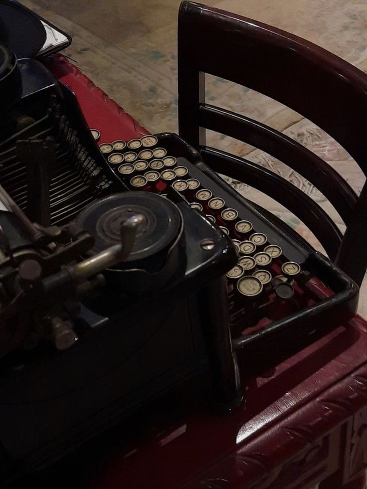 an old fashioned typewriter sitting on top of a wooden chair next to a red suitcase