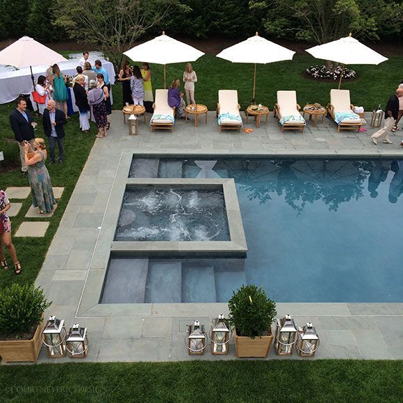 an aerial view of a pool surrounded by lawn chairs and umbrellas with people standing around it