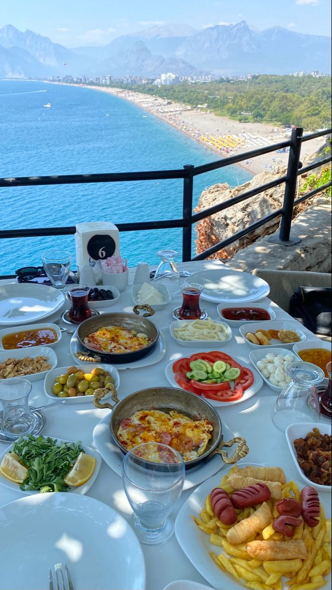 a table full of food on the side of a cliff overlooking an ocean and mountains