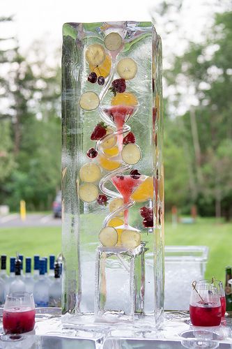 a tall glass vase filled with fruit and veggies sitting on top of ice