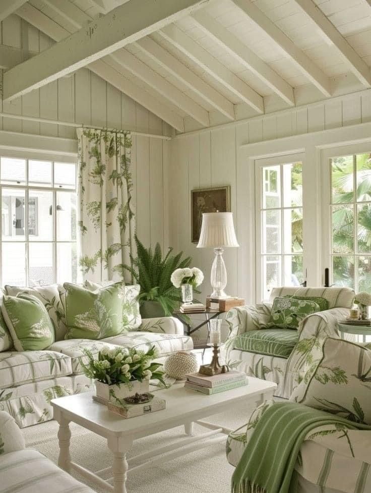 a living room filled with white furniture and green pillows on top of it's couches