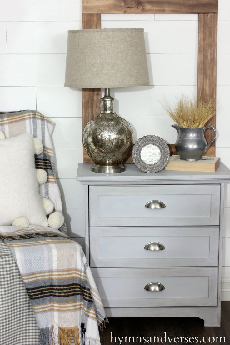 a nightstand with a lamp, plaid blanket and other items sitting on top of it