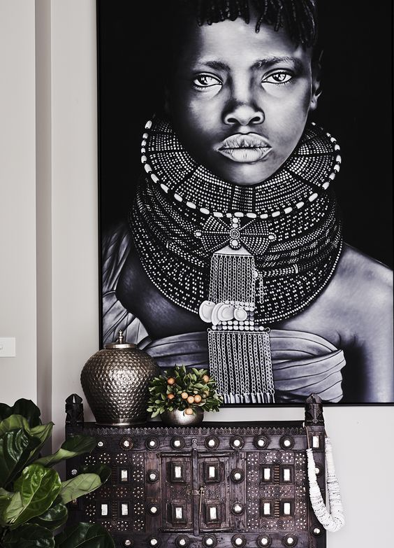 an african woman's portrait hangs on the wall above a chest of drawers