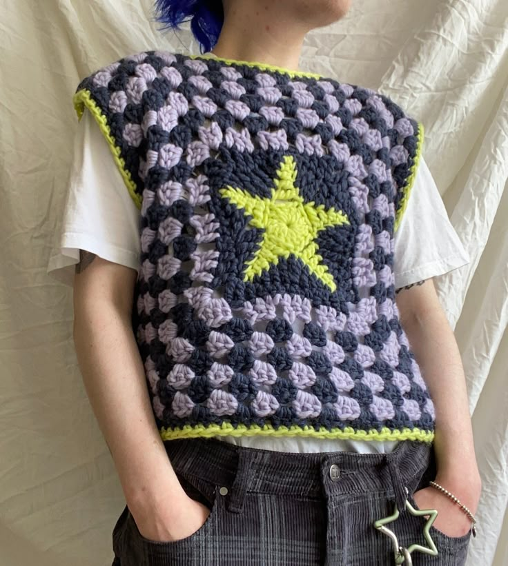 a woman with blue hair is wearing a crocheted star sweater and has her hands in her pockets