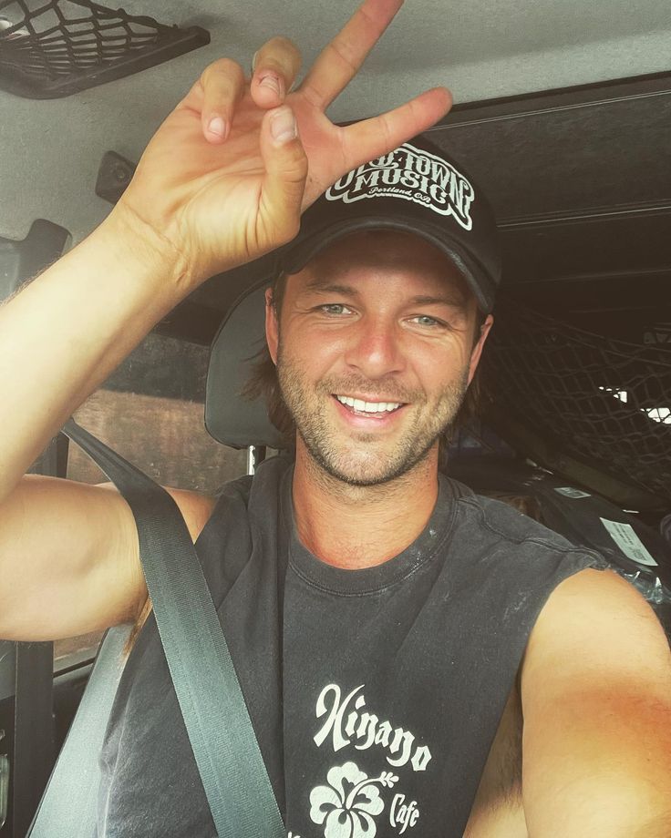 a man sitting in the back seat of a car holding up his peace sign with one hand