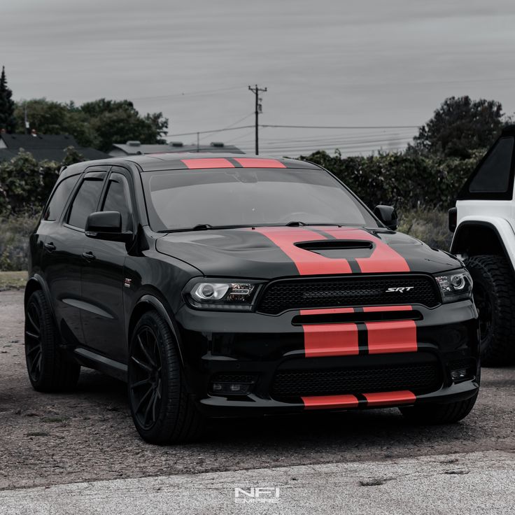 a black dodge truck with red stripes parked next to a white pickup truck