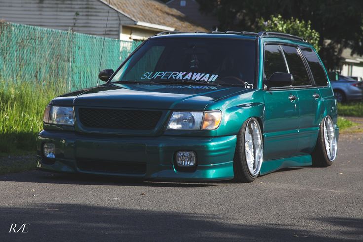 a green suv parked on the street in front of a fenced off area with grass