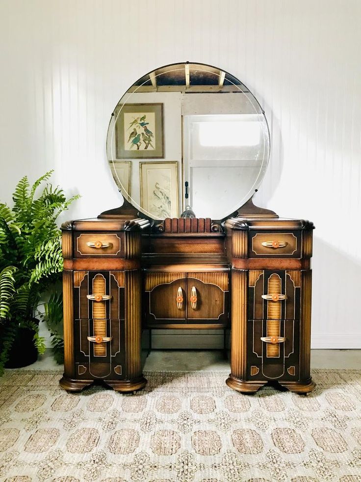 an antique vanity with mirror and potted plant on the floor in front of it