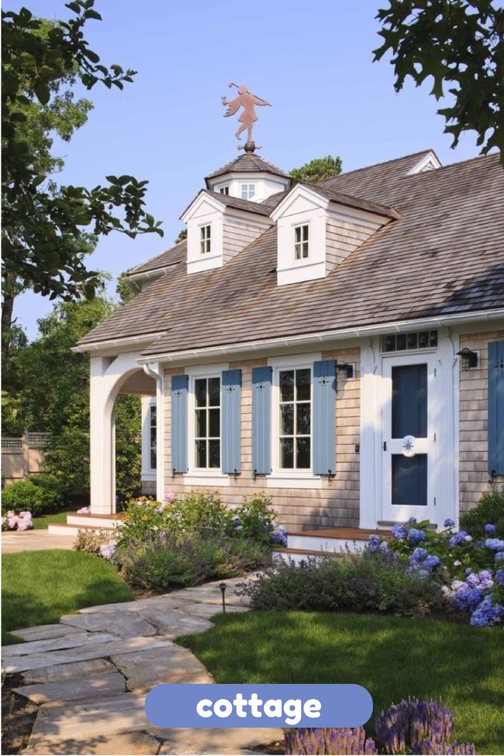 a small house with blue shutters and flowers in the front yard on a sunny day