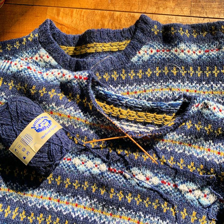 a blue sweater with yellow and red designs on it is next to a knitting needle