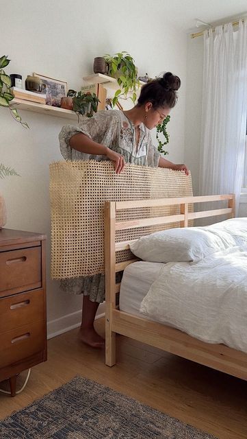 a woman standing next to a bed in a room with white walls and wooden floors