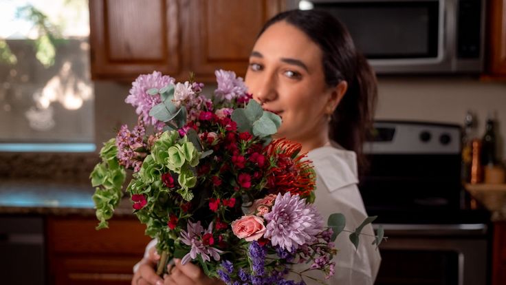 a woman holding a bunch of flowers in her hands and looking at the camera with surprise