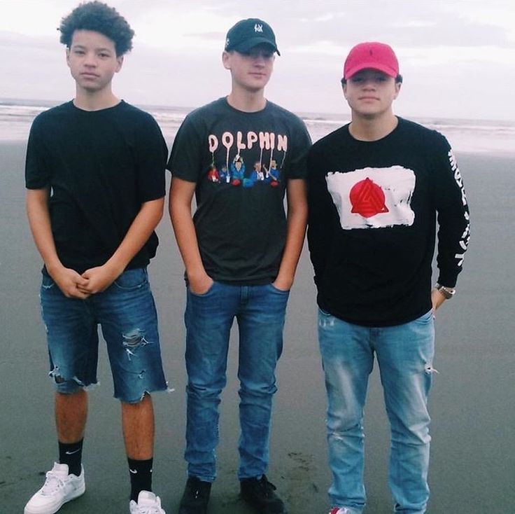 three young men standing next to each other on the beach