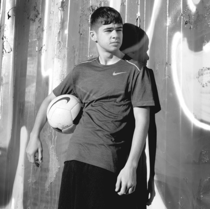 a young boy holding a soccer ball in front of a wall