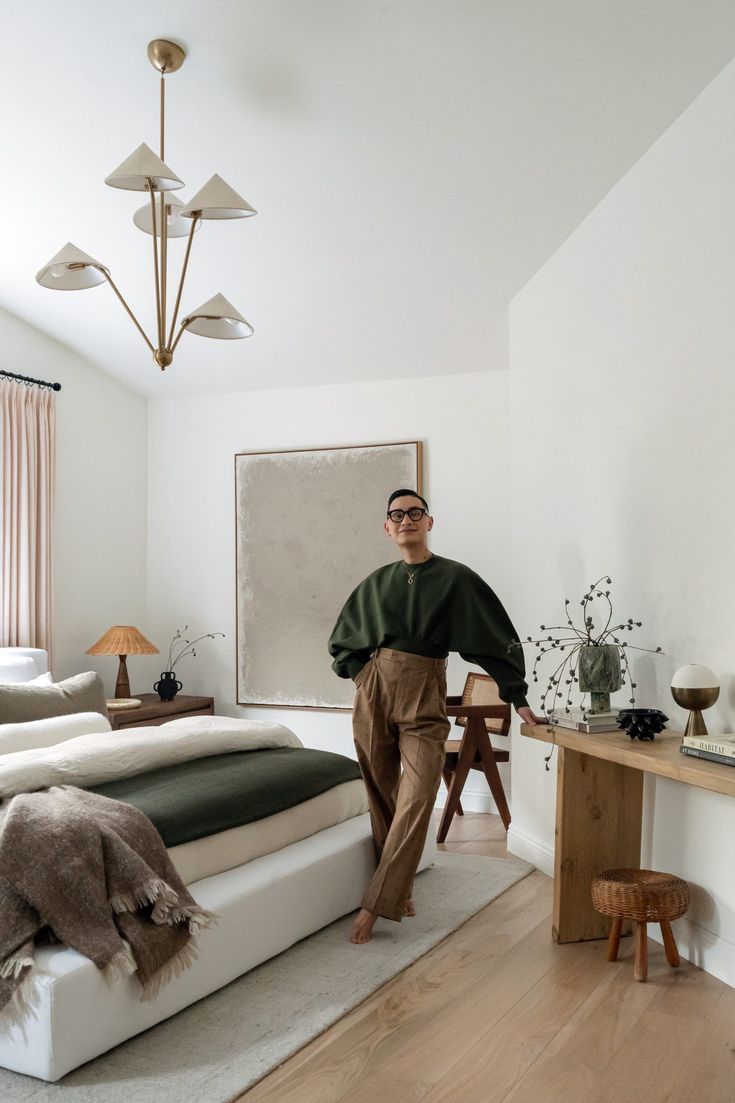 a man standing next to a bed in a room with white walls and wooden floors