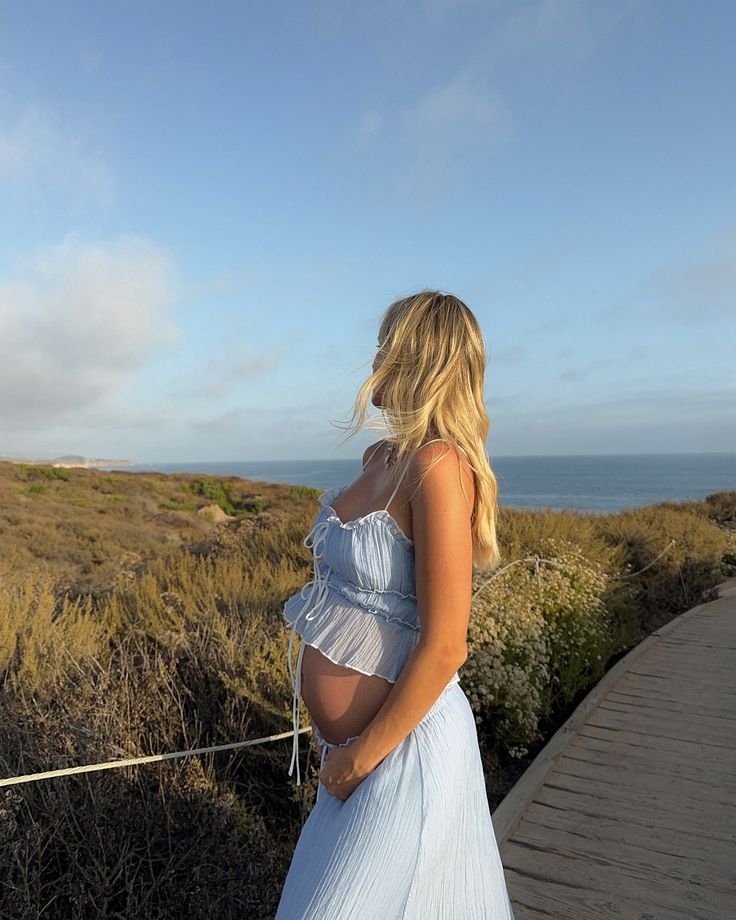 a woman in a white dress is standing on a wooden walkway by the ocean with her back to the camera