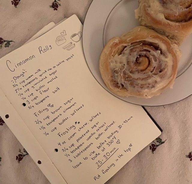 two cinnamon rolls sitting on top of a plate next to an open notebook with writing