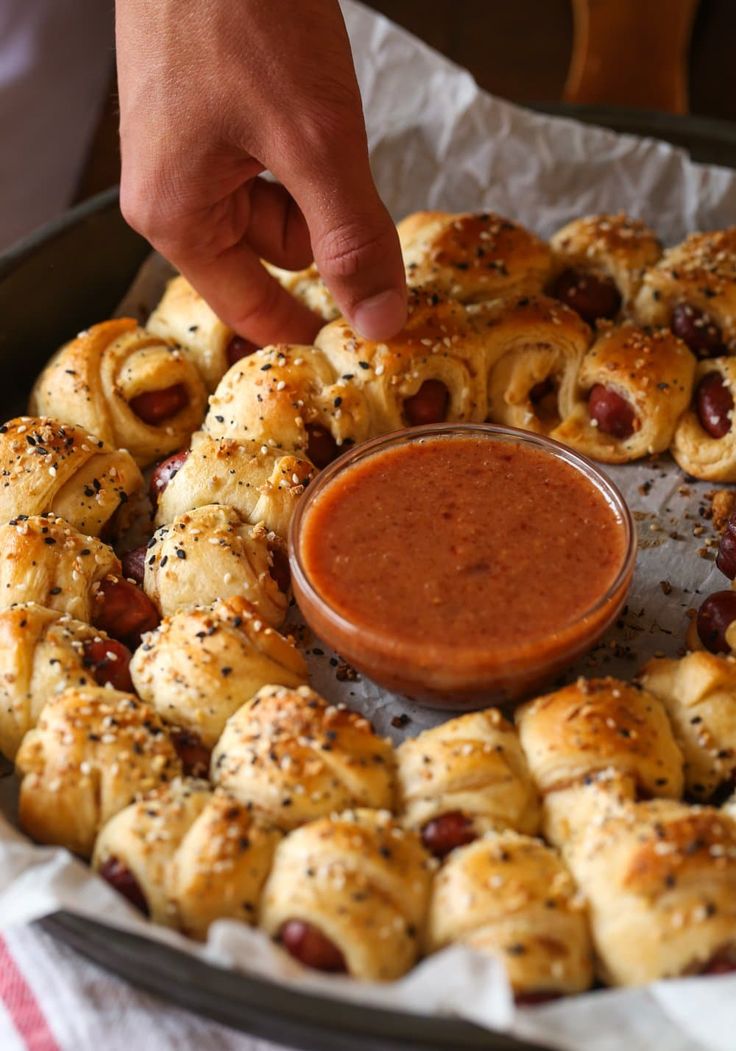 hot dogs wrapped in bread and topped with ketchup being dipping into a bowl