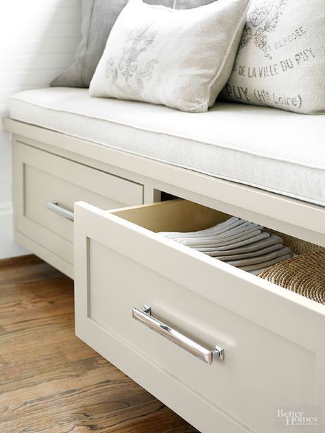 a white bench with drawers and pillows on it's seat, in front of a window