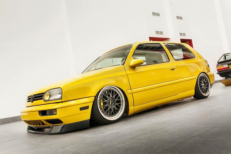 the yellow car is parked next to other cars in a room with white walls and flooring