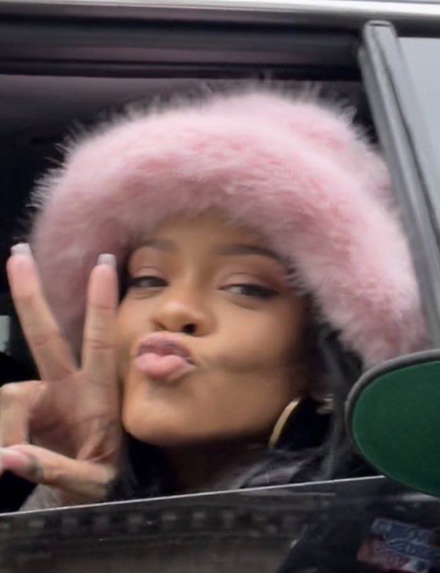 a woman in a car making the peace sign with her hand and wearing a pink fur hat