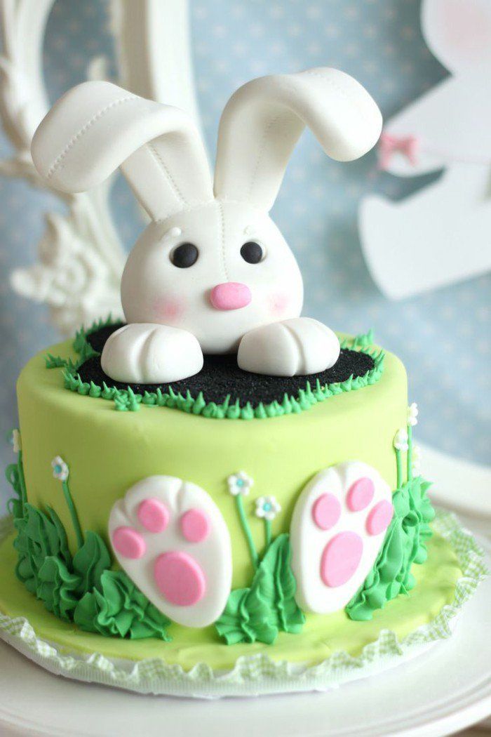 a green cake with white and pink decorations on it's sides, topped with a bunny figurine