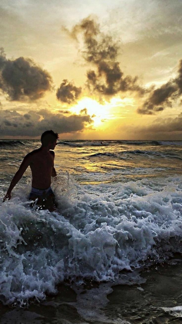 a man is wading in the ocean at sunset