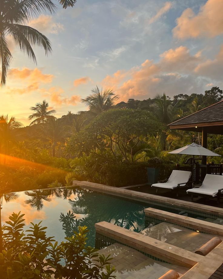 the sun is setting over an outdoor swimming pool with lounge chairs and umbrellas on it