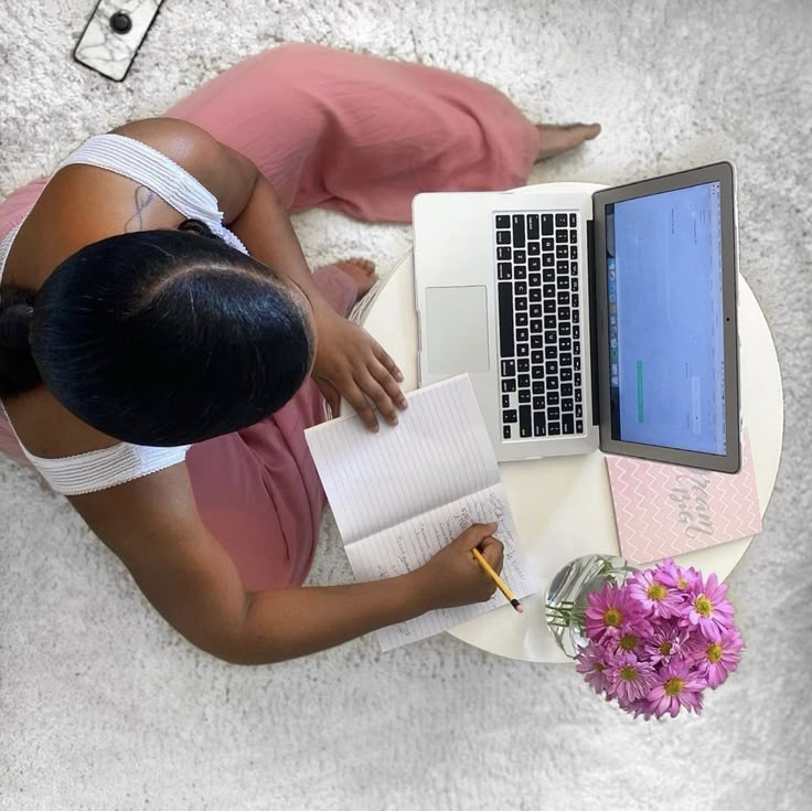 a woman sitting at a table with a laptop computer and notebook in front of her