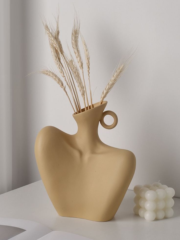 a vase with some dry grass in it on a table next to a white object