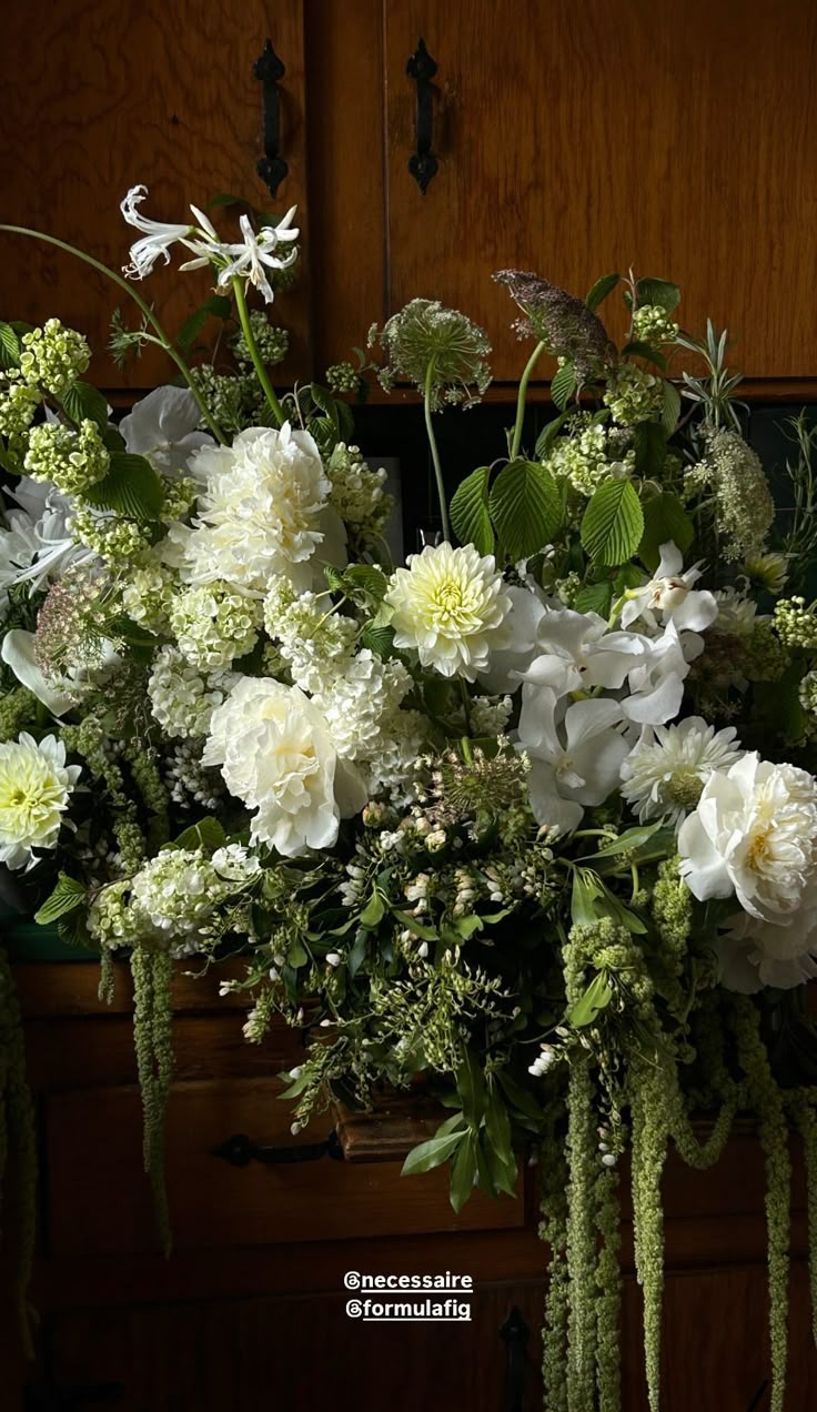 a bouquet of white flowers sitting on top of a wooden table next to a cabinet