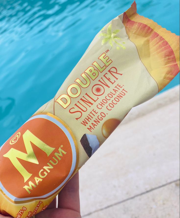 a person holding up a mcdonald's doughnut next to a swimming pool with water in the background