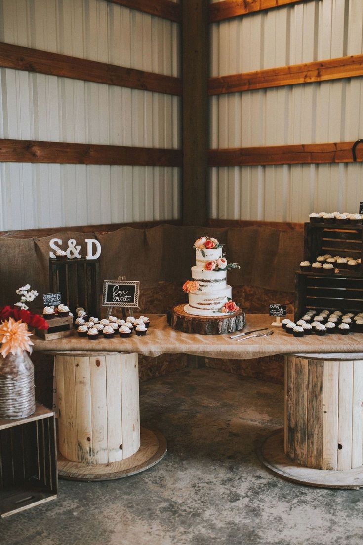 a table with cupcakes and cakes on it at a wedding reception in a barn