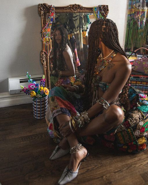 a woman sitting on the floor in front of a mirror with braids and jewelry