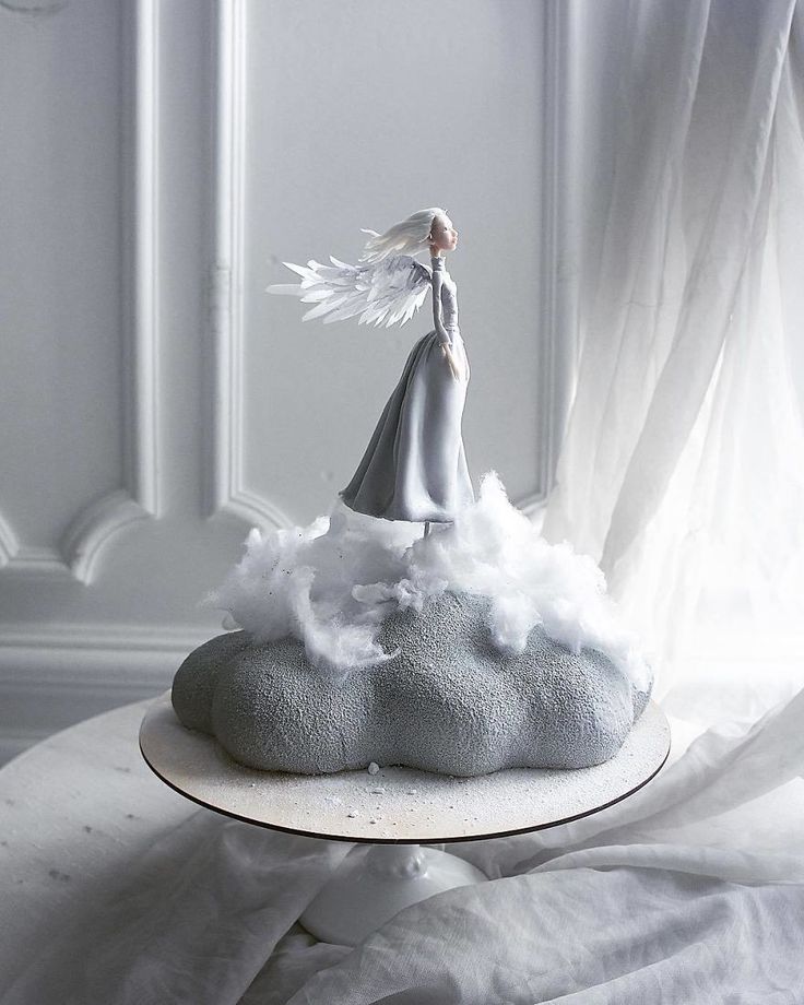 an angel figurine sitting on top of a cloud covered cake