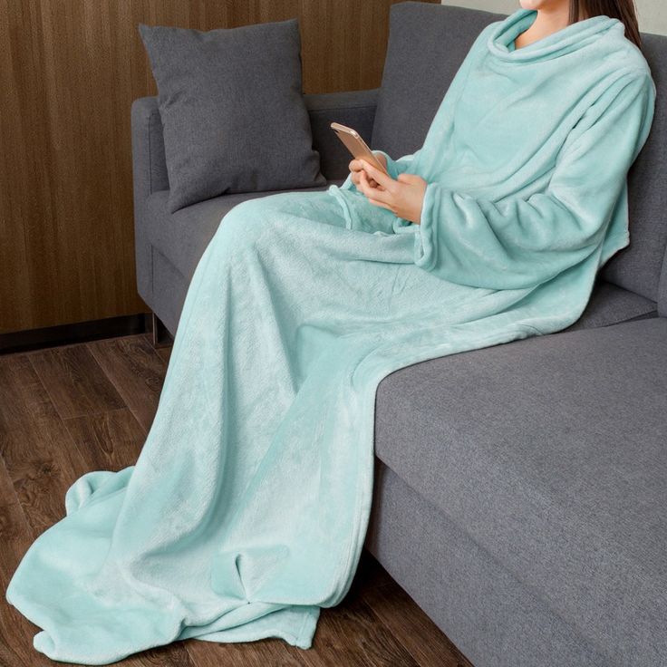 a woman sitting on a couch under a blanket using a cell phone while wrapped in a blanket