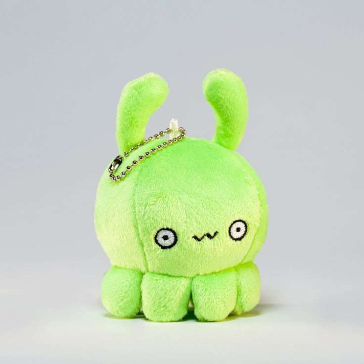 a green stuffed animal with a tiara on it's head, sitting in front of a gray background