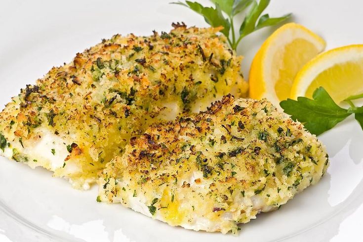 two pieces of chicken on a white plate with lemon wedges and parsley sprigs