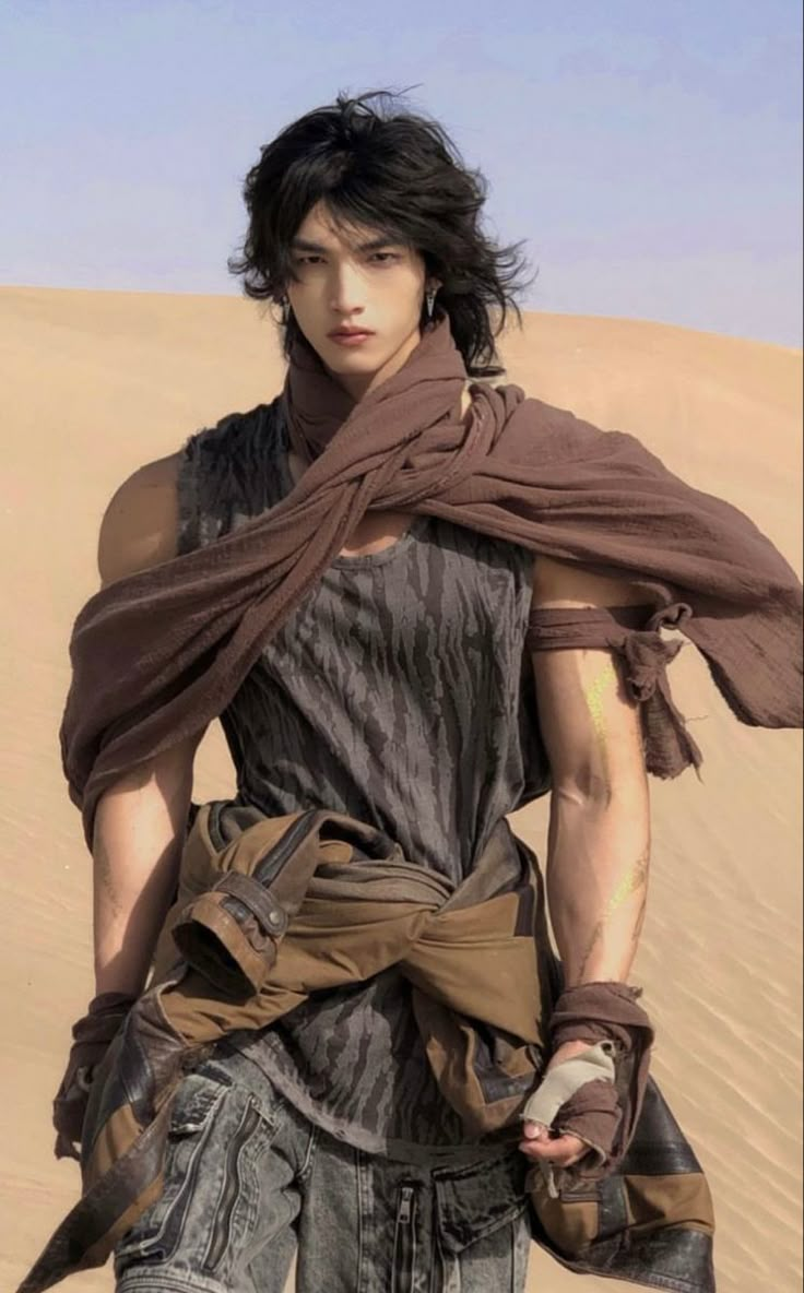 a young man in the desert with his hands on his hips and wearing a scarf around his neck